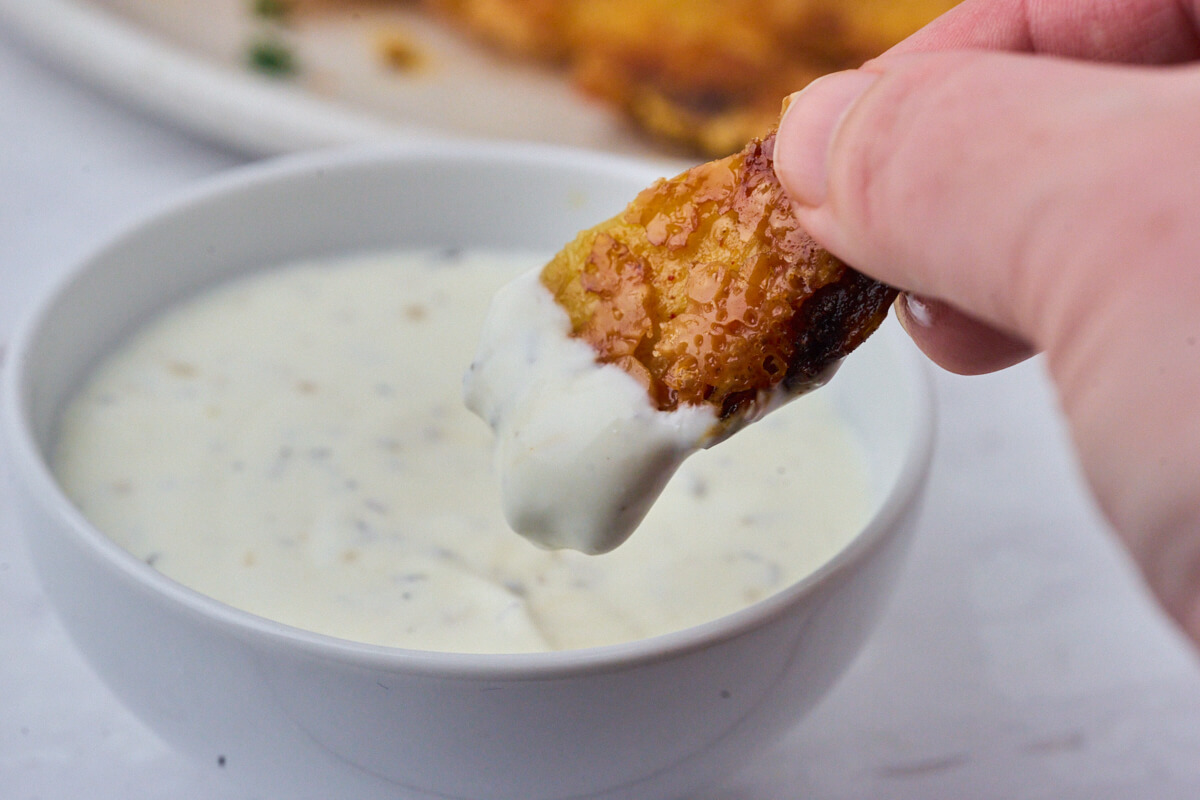 crispy parmesan-crusted potato being dipped in sour cream dip. 