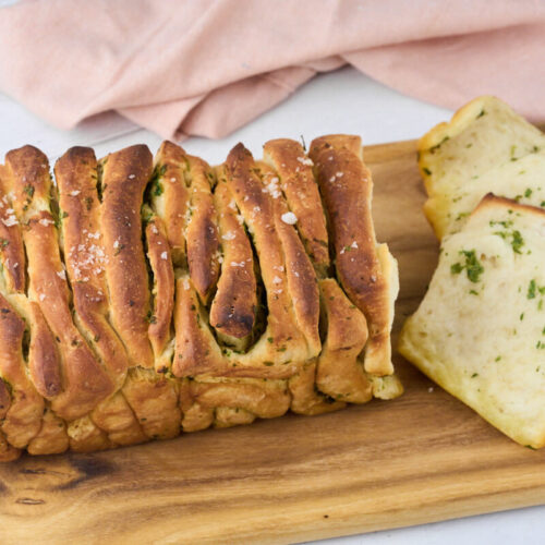 pull apart garlic bread with parsley on a wooden chopping board ready to be served.