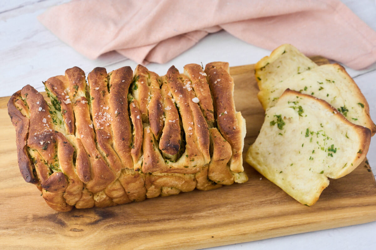 pull apart garlic bread with parsley on a wooden chopping board ready to be served.